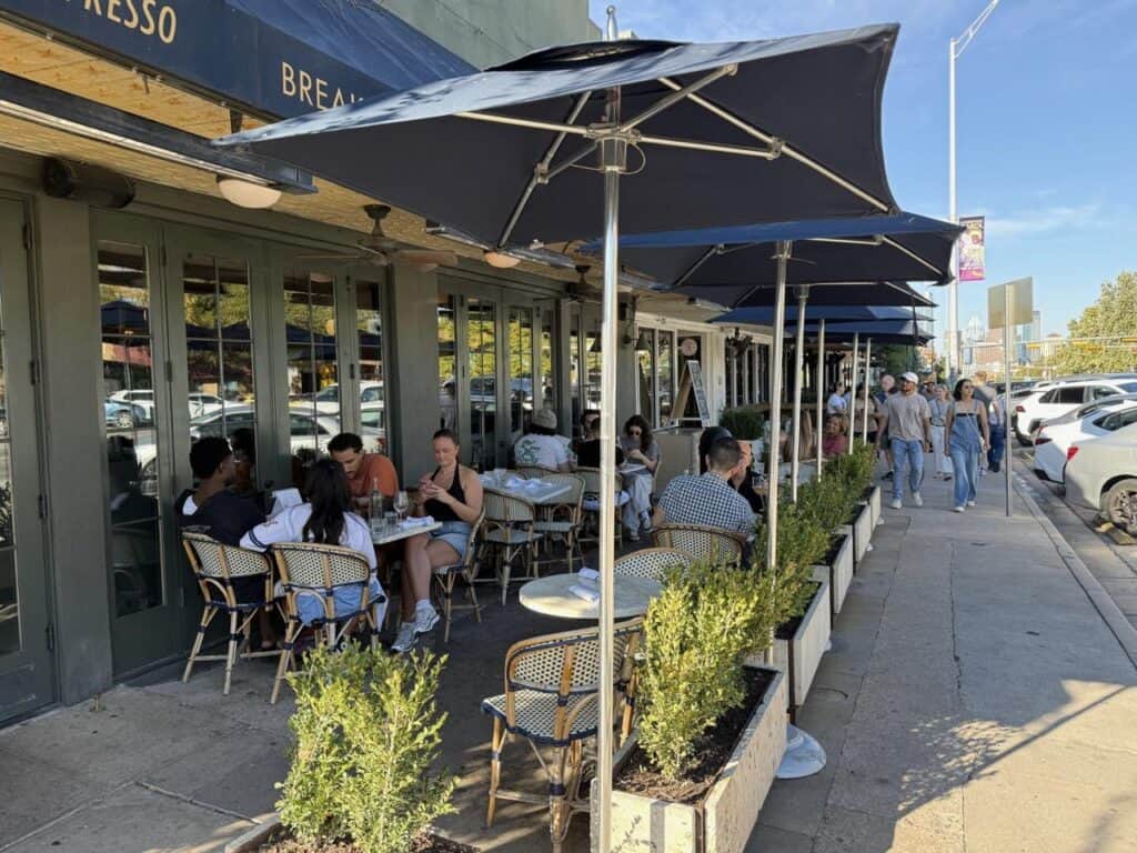 Diners at a shaded sidewalk patio on South Congress Avenue in Austin with the downtown skyline behind