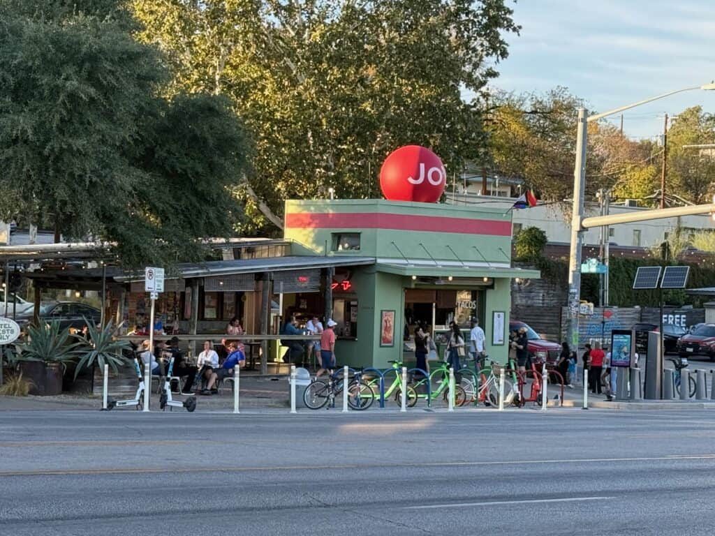 Jo's Coffee walk-up window and shaded patio on South Congress Avenue in Austin, with bikes and scooters parked at the curb