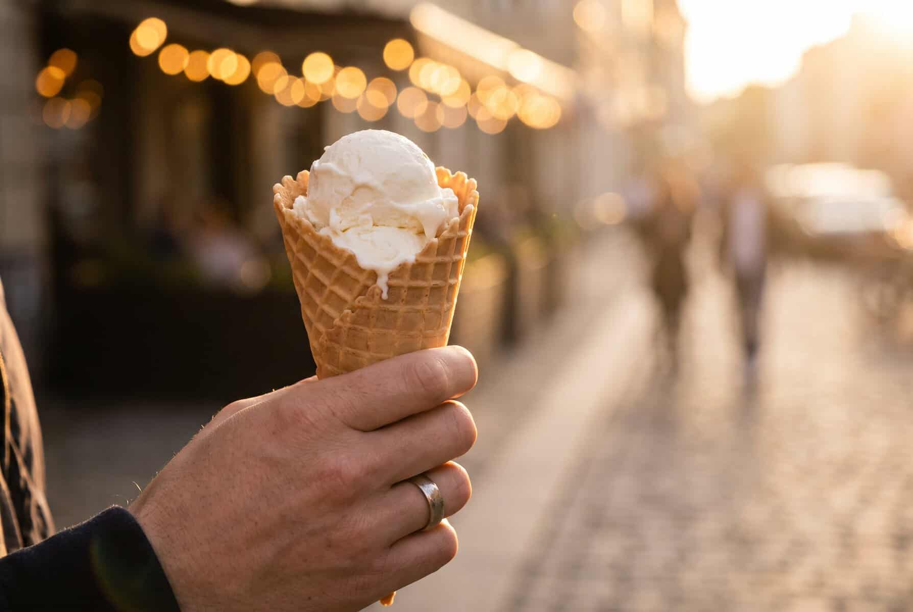 A waffle cone of ice cream held up on a sunlit South Congress street