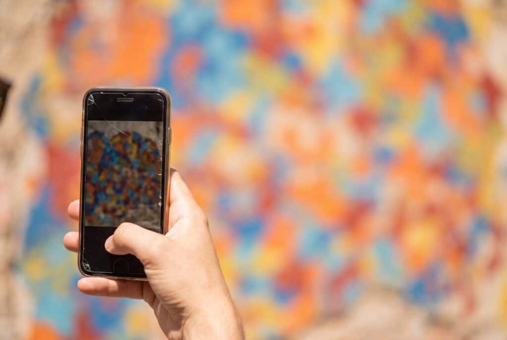 A visitor photographing a brightly painted mural wall on South Congress with a phone